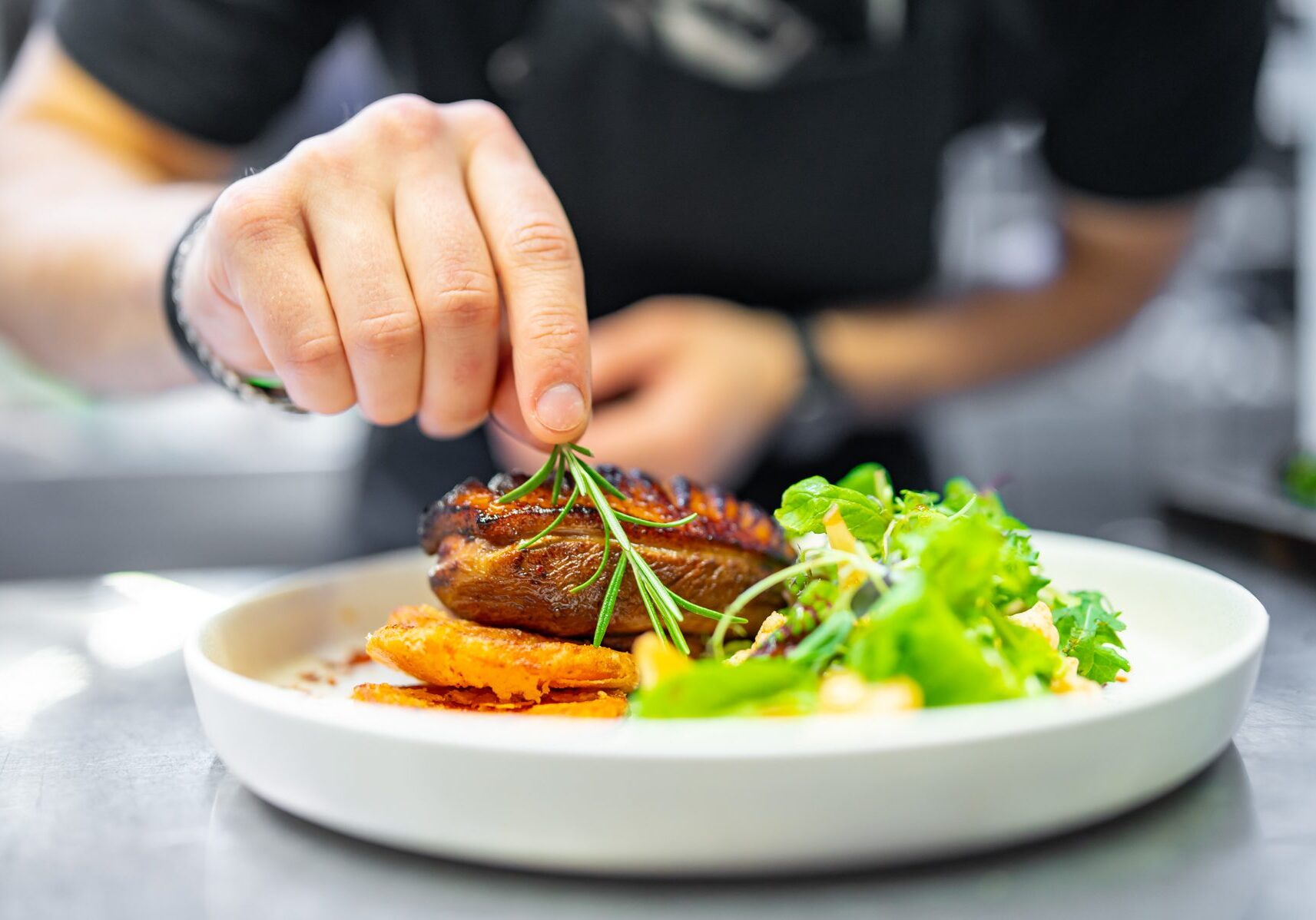 chef hand cooking Roasted Duck breast fillets with vegetable salad and batat in plate on restaurant kitchen